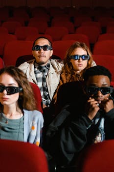 Diverse group of young adults enjoying a 3D movie in a theater with red seats.
