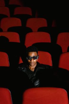 Man in 3D glasses watching a movie alone in an empty theater with red seats.