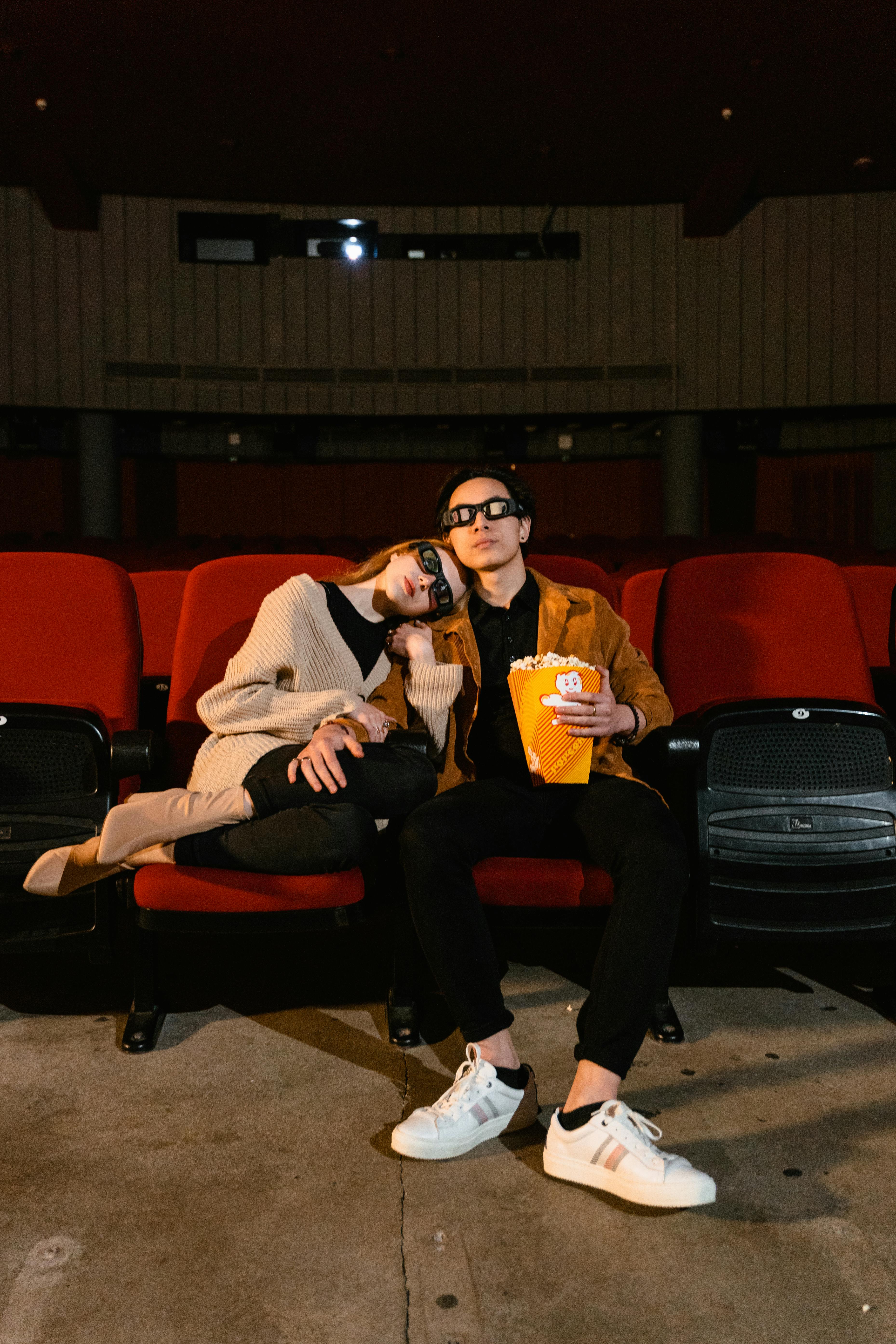 Free A couple sitting in an empty theater enjoying a movie with popcorn. Stock Photo