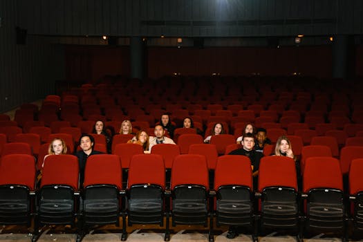 A group of people watching a movie in a nearly empty cinema theater with red seats.