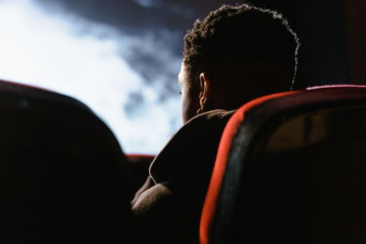 A person sits in a theater watching a movie on a large screen, enveloped in a dark ambiance.
