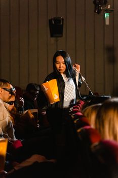 Young Asian woman seated in a cinema, holding popcorn, enjoying a movie.