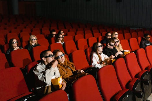 People in 3D glasses watching a movie in a theater with popcorn and red seats.