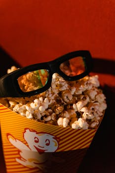 Bucket of popcorn with 3D glasses in a cinema setting, ready for movie night excitement.