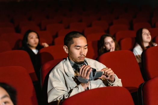 A man uses a camcorder in a sparsely attended movie theater, focusing on audience experience.