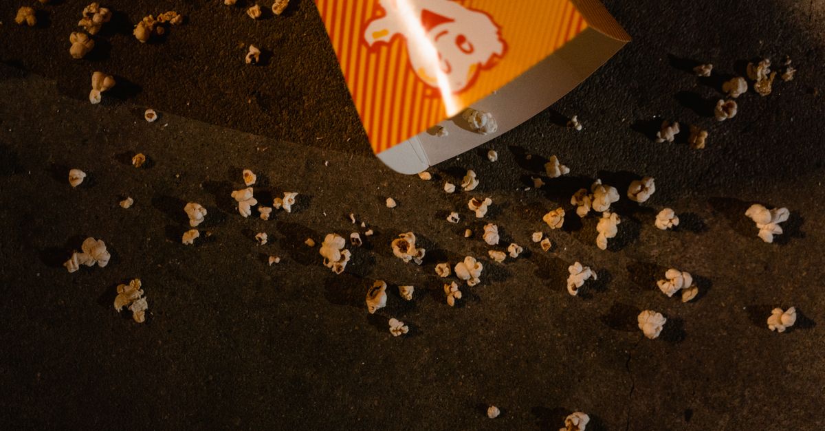 Overturned popcorn tub on floor with scattered popcorn, high angle view.