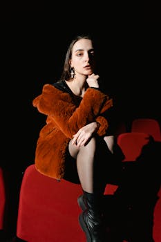 Elegant woman in a fur coat sitting in a theater, posing thoughtfully.