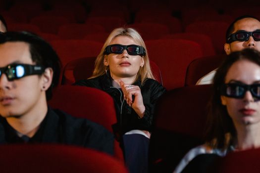 Diverse group of adults wearing 3D glasses in a cinema, focused on screen.