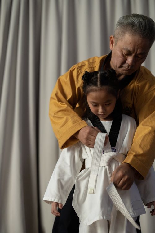 Free A martial arts instructor assisting a young student with her karate belt, demonstrating skill and patience. Stock Photo