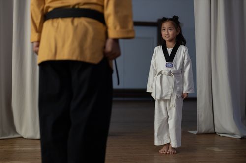 Free Young girl standing in martial arts uniform facing an instructor during a training session. Stock Photo