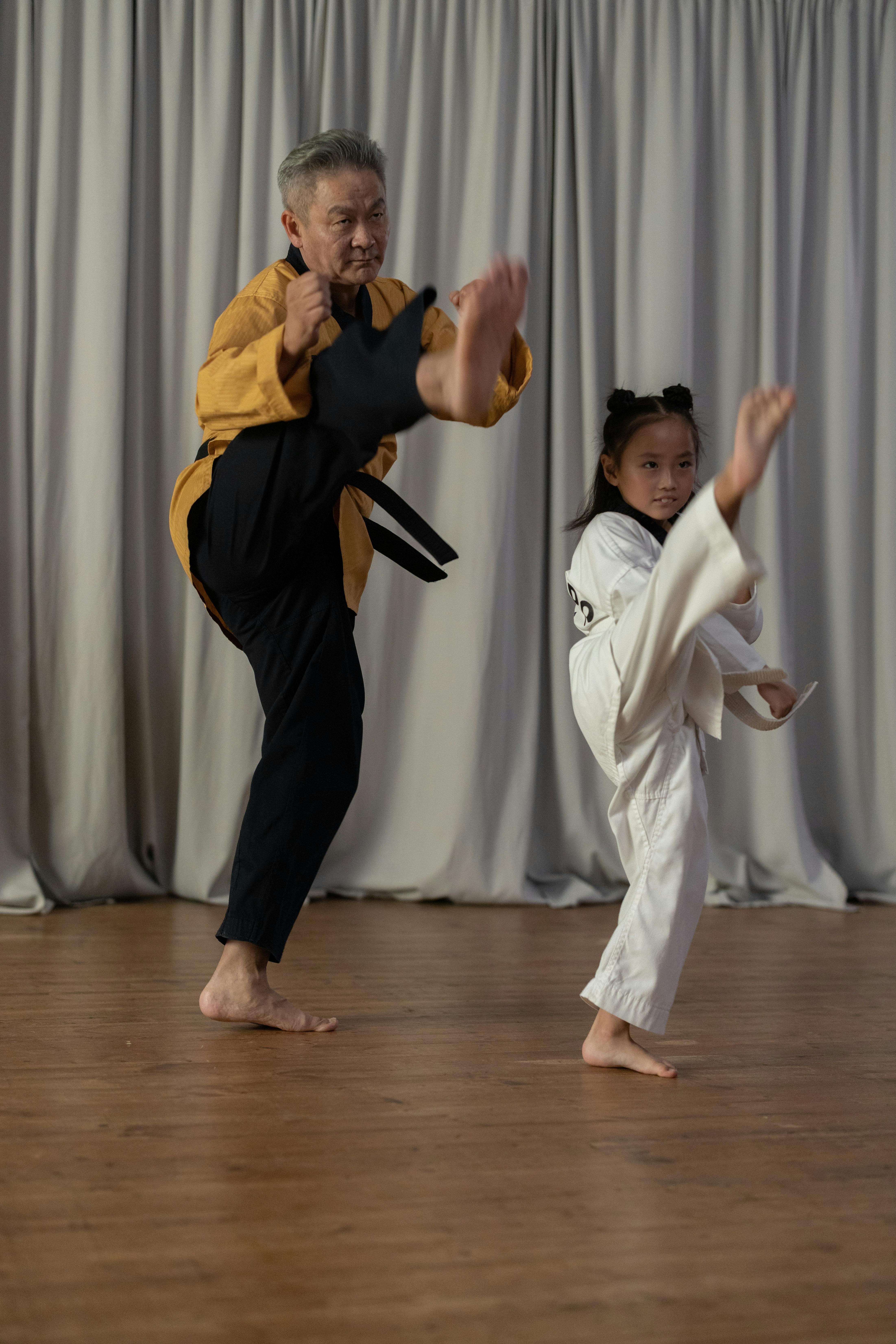 a girl and a mature man wearing karate uniforms kicking on air