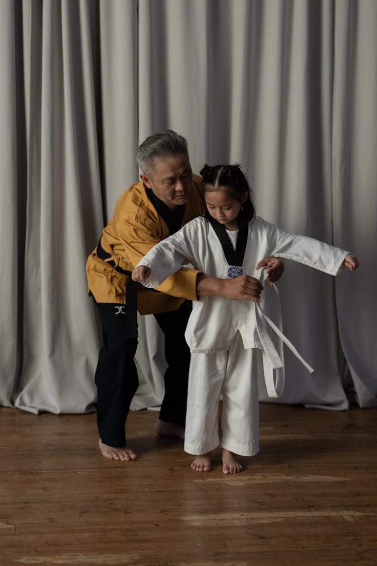 A Martial Arts Instructor Putting A White Belt On A Kid