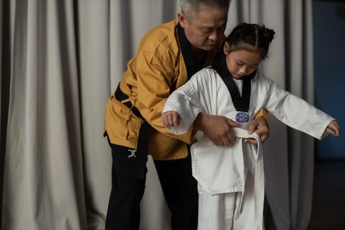 Free Elderly man instructs young girl in martial arts indoors, wearing uniforms. Stock Photo