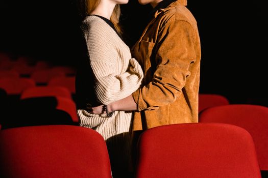 Young couple hugging in red-seated cinema, enjoying a romantic date night indoors.