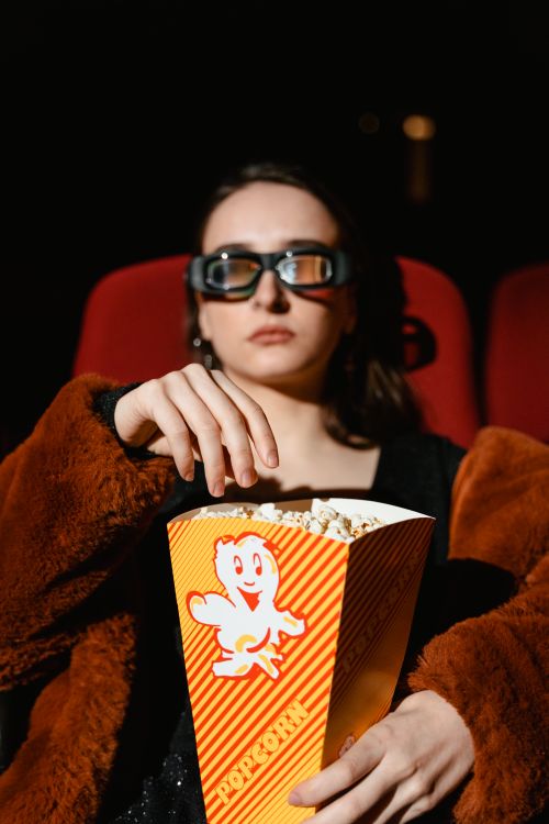 Free Woman wearing 3D glasses, enjoying popcorn during a movie in a cinema setting. Stock Photo