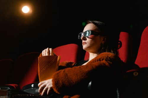 Free A woman watching a 3D movie in a theater, wearing glasses and holding popcorn. Stock Photo