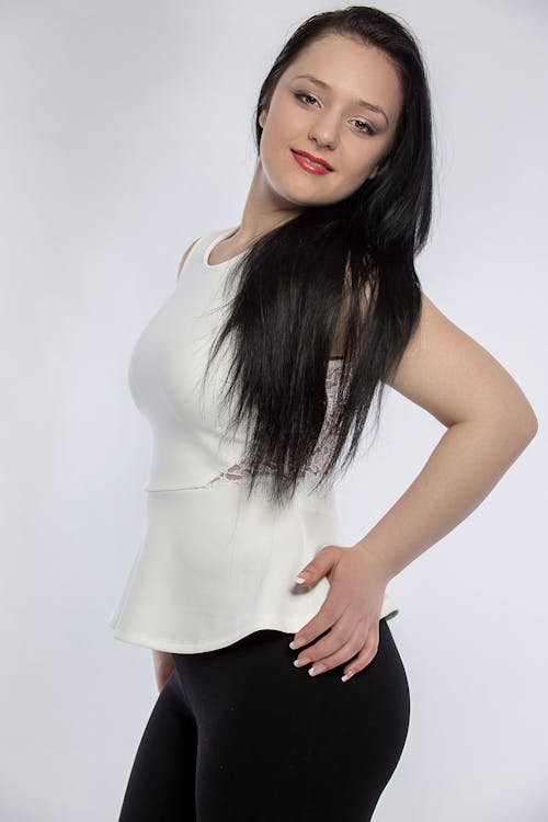 Studio Shot of a Young Brunette Wearing a White Top and Black Pants Posing on White Background 