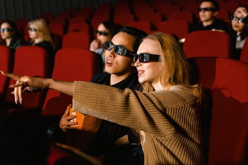 Free A couple wearing 3D glasses enjoy a movie at a theater, immersed in the experience. Stock Photo