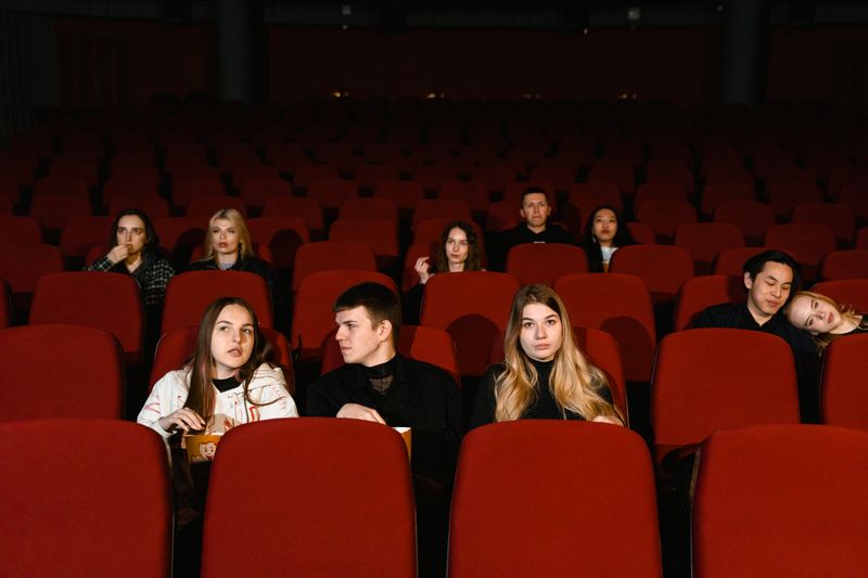 Audience members watching a film in a darkened cinema with red seats and popcorn