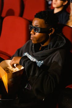 Man wearing 3D glasses enjoying popcorn while watching a movie in a cinema setting.