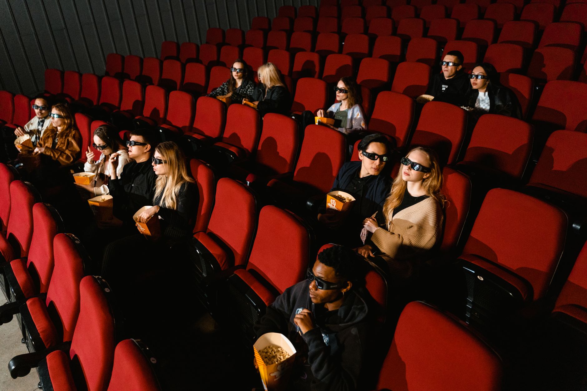 People enjoying a film in a cinema, wearing 3D glasses and eating popcorn.