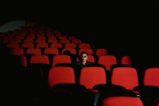 A person sits alone in a dimly lit auditorium with striking red seats.