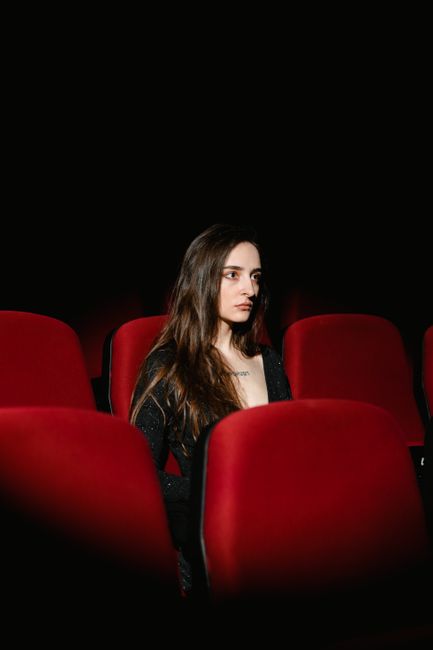 A woman sits alone in an empty movie theater with red seats and a dark ambiance.