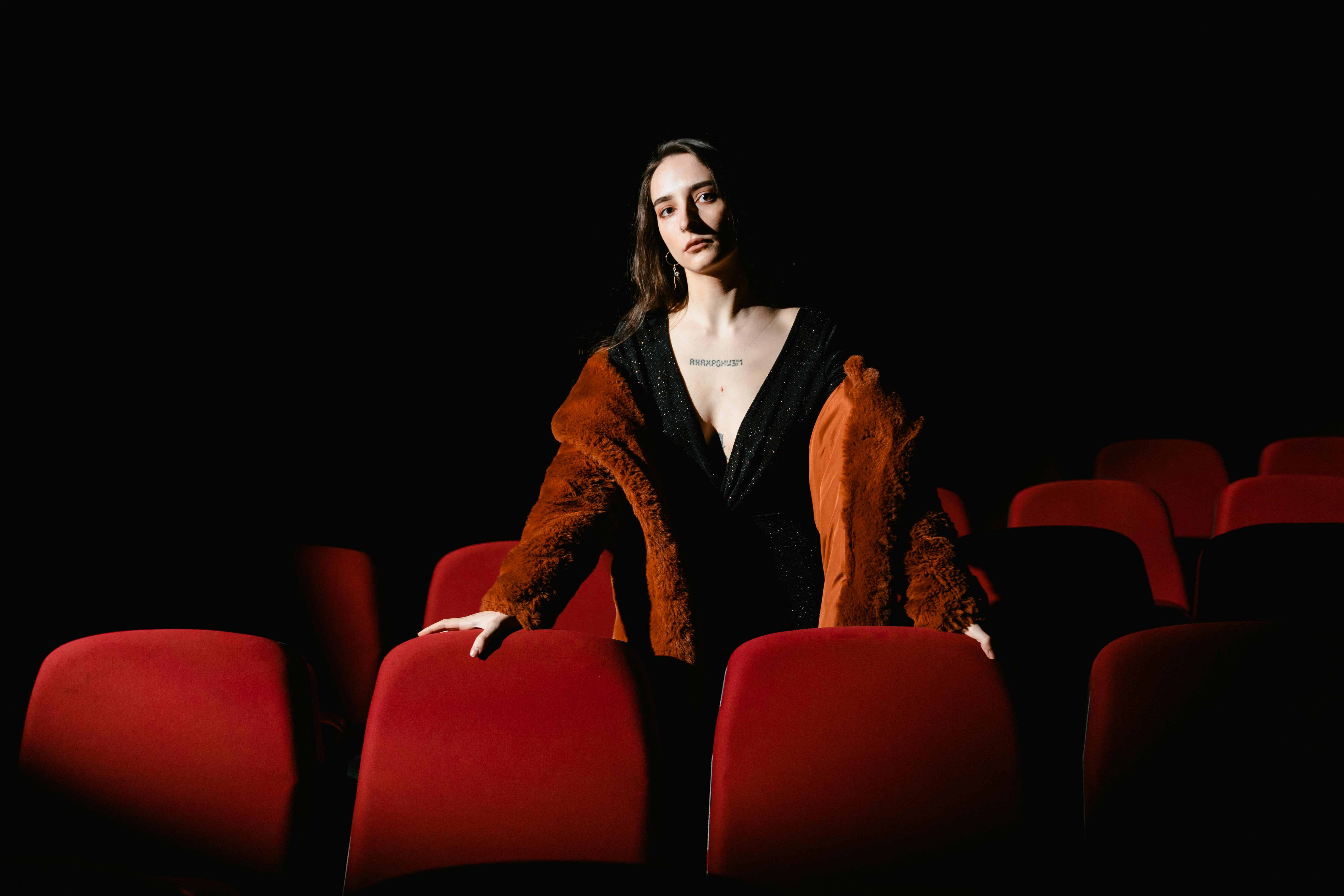 Free Stylish woman in a coat stands in an empty cinema with red seats, exuding elegance. Stock Photo