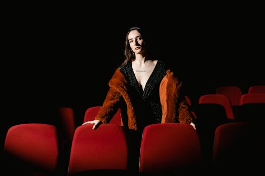 Stylish woman in a coat stands in an empty cinema with red seats, exuding elegance.