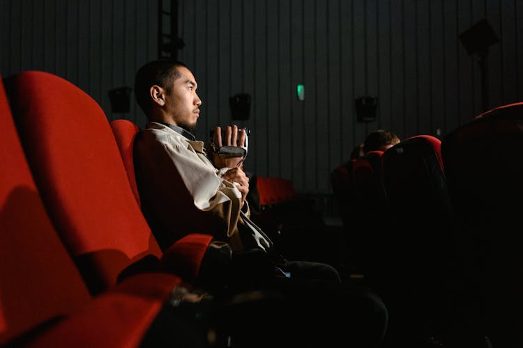 Side View Of A Man Sitting In A Cinema And Watching A Movie 