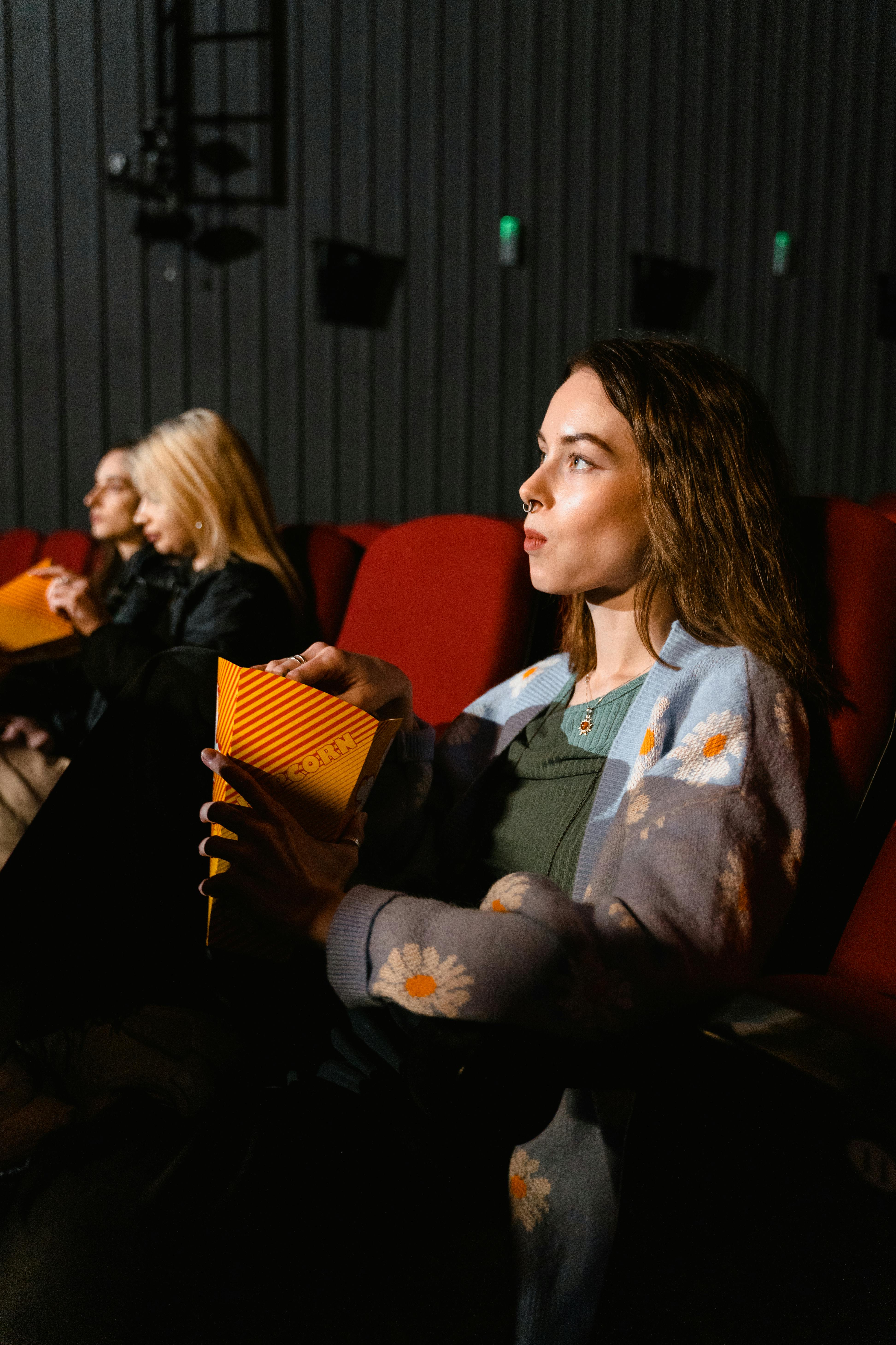 A woman enjoys popcorn while watching a film in a cozy cinema setting. Perfect for entertainment themes.