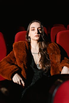Woman in a fur coat sitting in a movie theater, backlit by dramatic light.