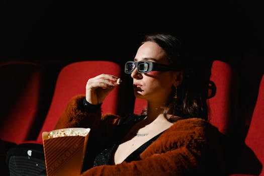 A woman enjoying a cinema experience wearing 3D glasses, holding popcorn.