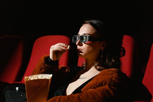 Free A woman enjoying a cinema experience wearing 3D glasses, holding popcorn. Stock Photo
