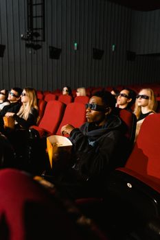 A group of adults watching a 3D movie in a theater, wearing 3D glasses and enjoying popcorn.