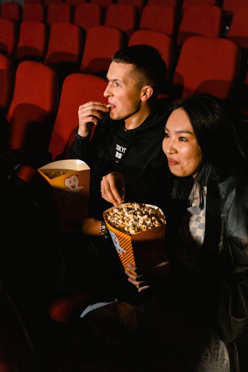 Free Man and Woman Eating Popcorn While Sitting in a Cinema Stock Photo