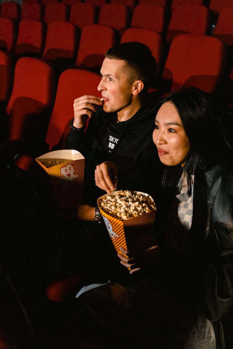 Man And Woman Eating Popcorn While Sitting In A Cinema