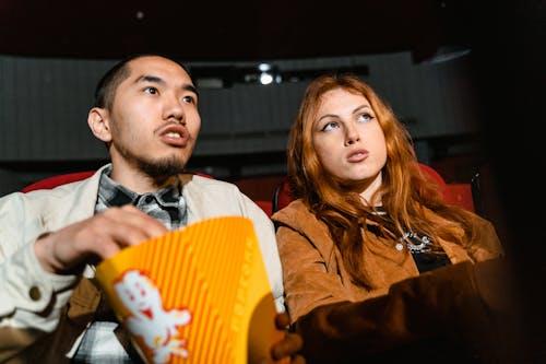 Free A Woman Sitting Next to a Man Holding a Popcorn Box Stock Photo
