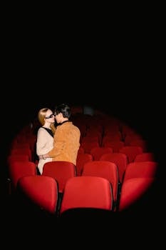 A couple kissing in a movie theater surrounded by red seats under a spotlight.