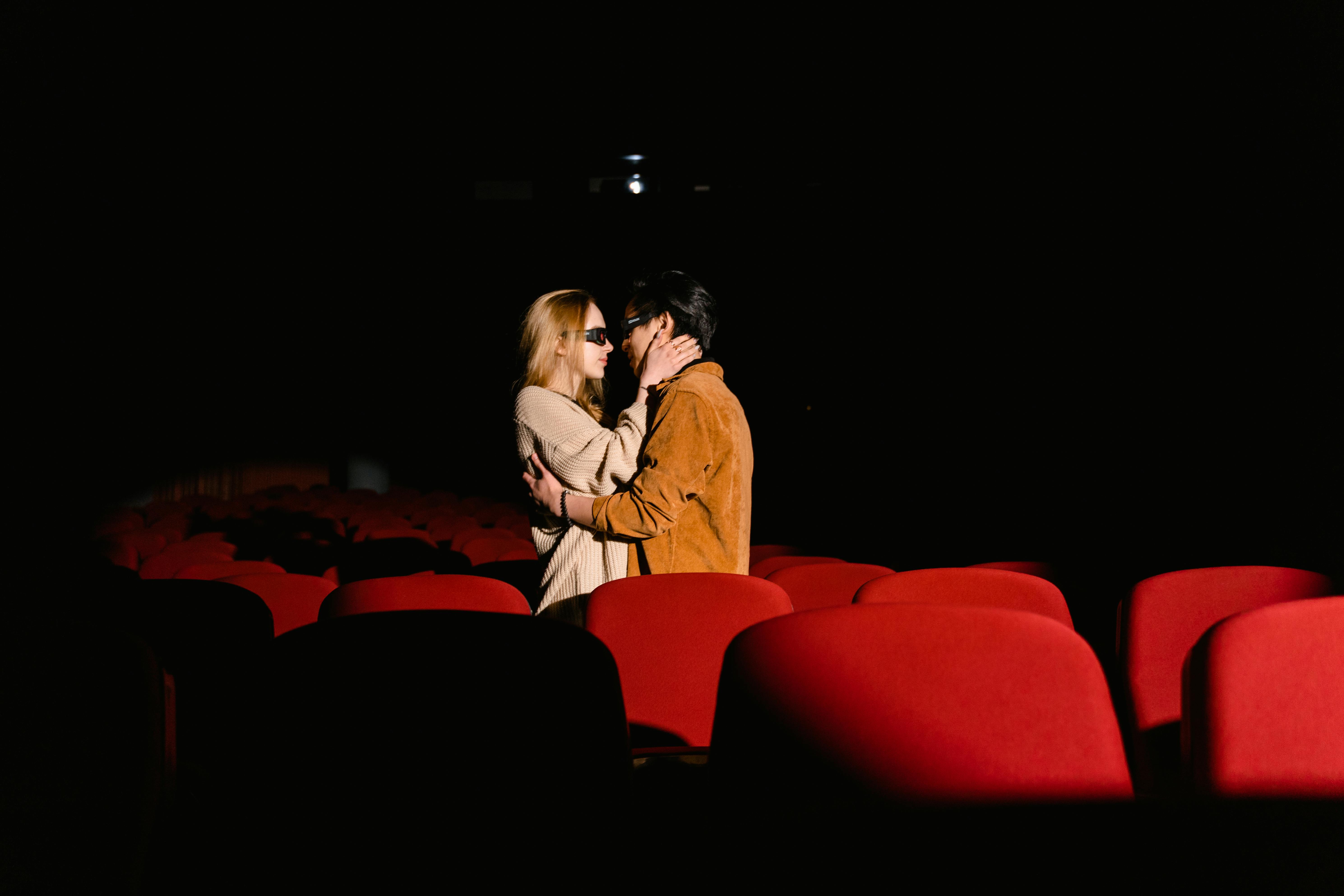 Free Couple sharing a tender moment in an empty movie theater with red seats. Stock Photo