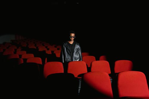 Free A stylish individual in a leather jacket stands amidst empty theater seats. Stock Photo