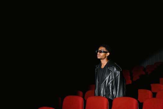 Individual in 3D glasses and leather jacket at an empty movie theater.