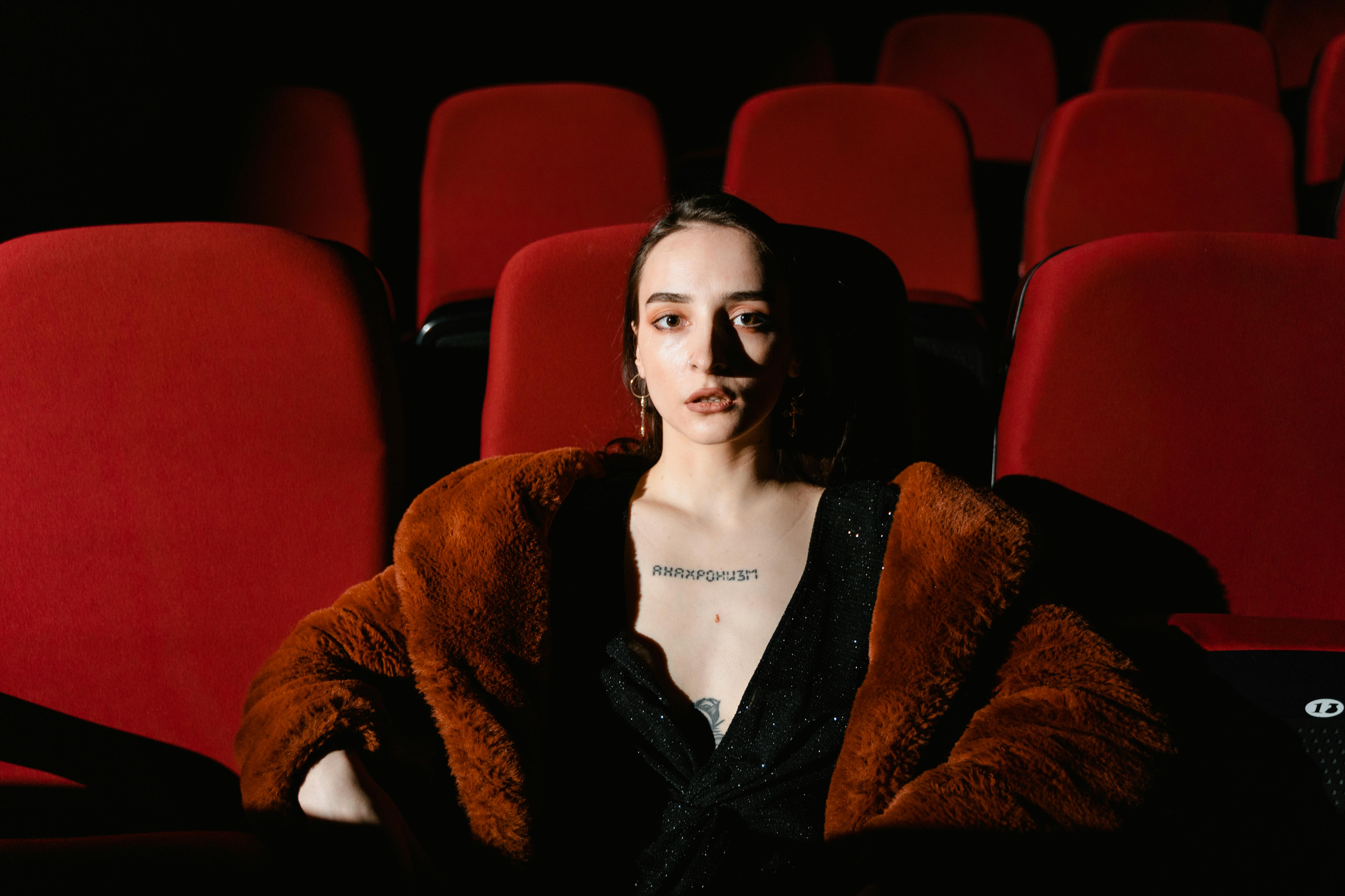 Free A stylish woman wearing a fur coat sits confidently in a dimly lit theater. Stock Photo