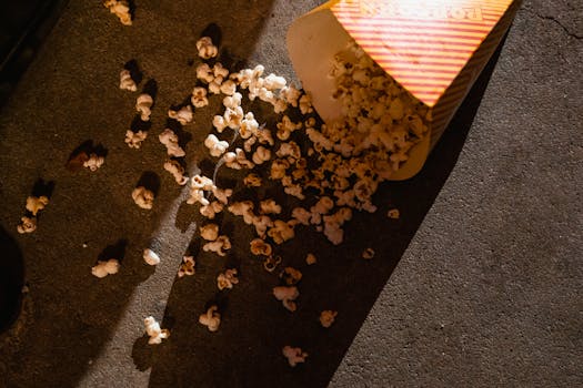 A box of popcorn spilled on a concrete floor under dim lighting, creating a casual snack-time scene.