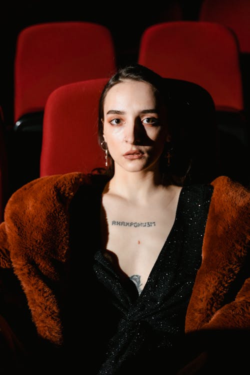 A Woman in Brown Fur Coat Over a Black Glittering Dress Sitting on a Red Chair