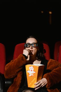 A woman in 3D glasses enjoying popcorn while sitting in a cinema seat during a movie.