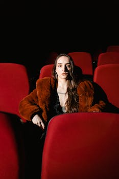 Stylish woman in a fur coat sitting in a dimly lit movie theater. Fashionable and cinematic vibe.