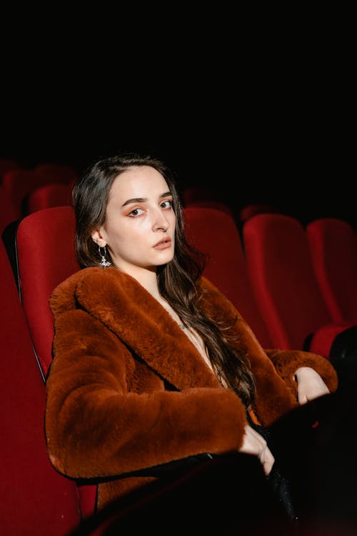 A Woman in Brown Fur Coat Sitting on a Red Chair