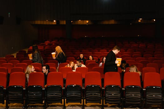 Group of people enjoying a movie with snacks in a cinema with red seats.