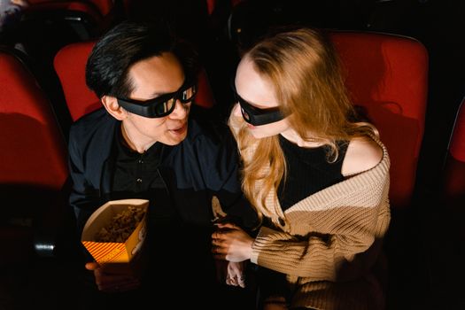 A couple wearing 3D glasses enjoying a movie with popcorn in a cinema.